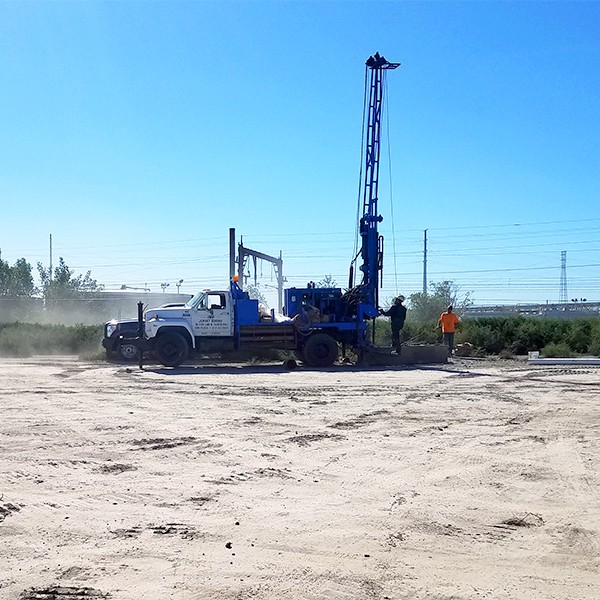 blue truck with soil boring drill in distance on sandy ground with blue sky