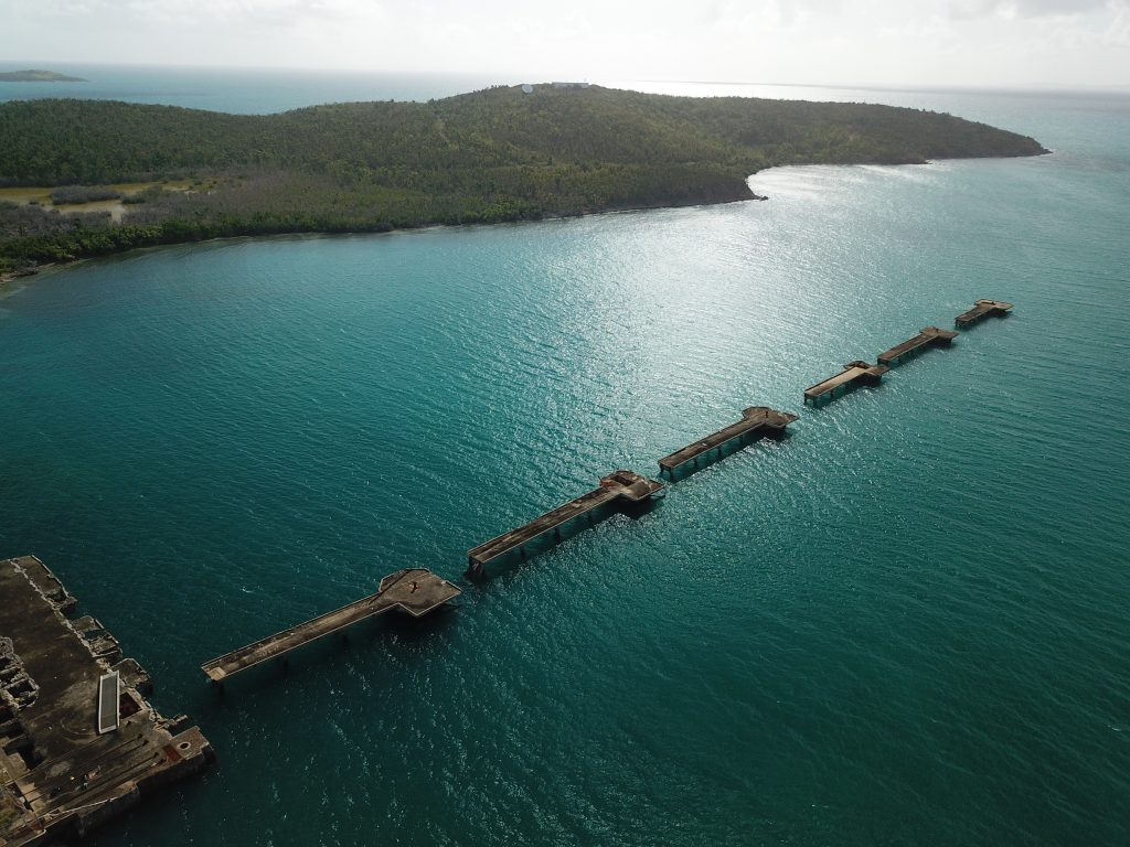 aerial shot of broken pier in puerto rico with turquoise water and green hills in the background