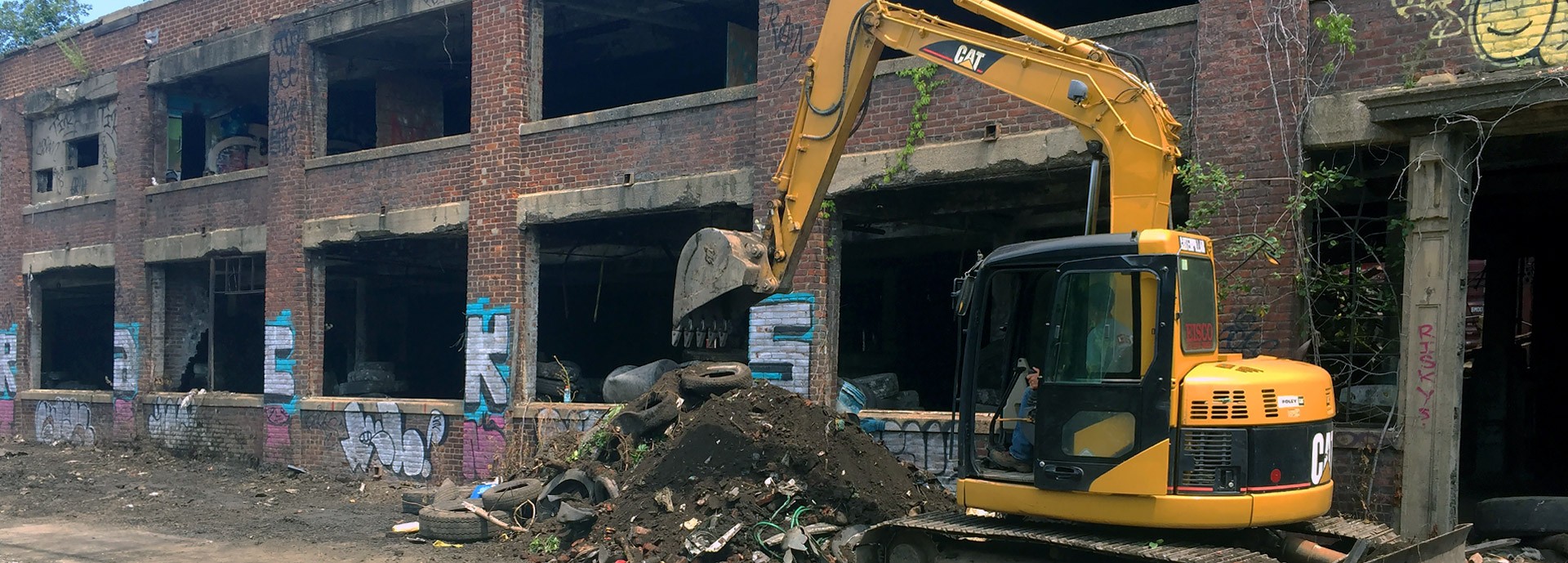 excavator in front of abandoned brick building and pile of dirt