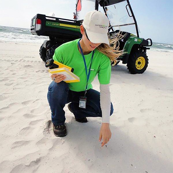 woman in green shirt bending down to the sand with harm extended with truck in background on beach