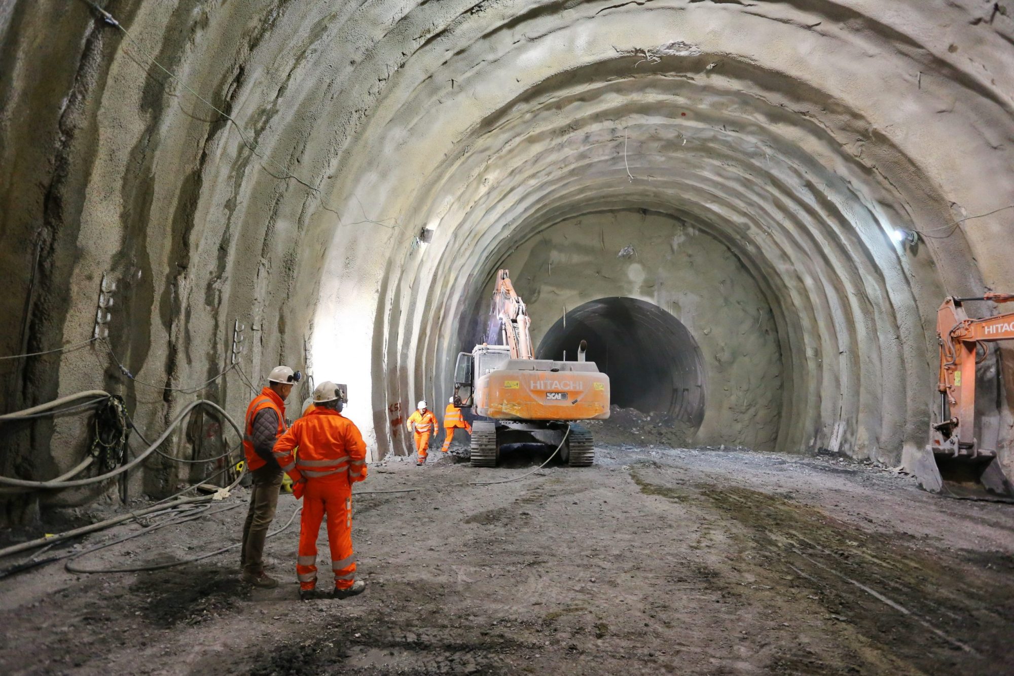 workers in large tunnel with excavator in background