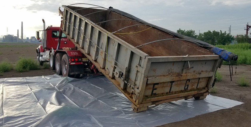 dumpster being loaded off a truck onto a tarp with grasses in the background