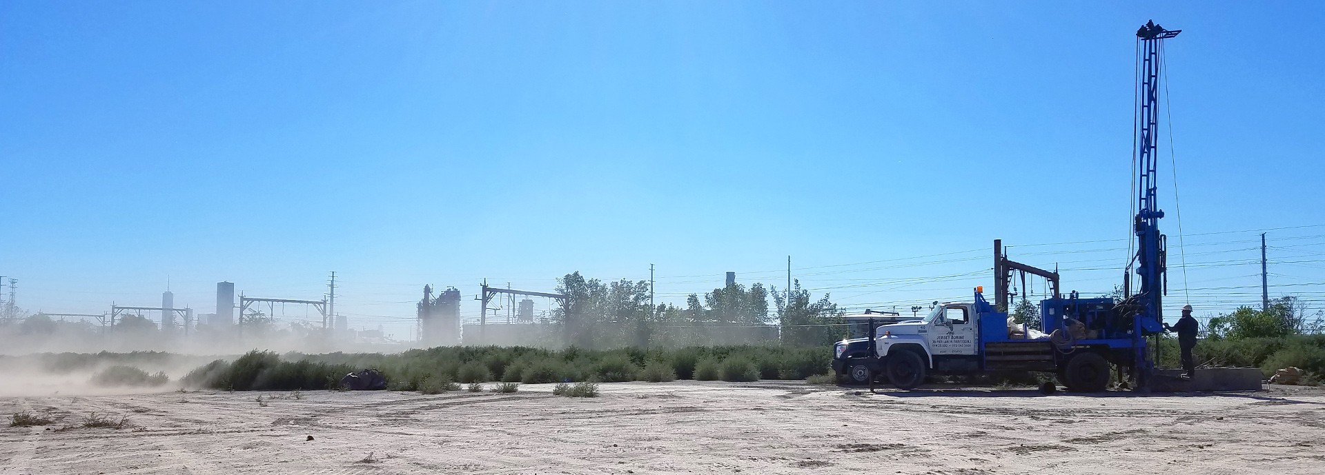 soil drilling equipment on sandy dirt terrain with blue sky near train tracks