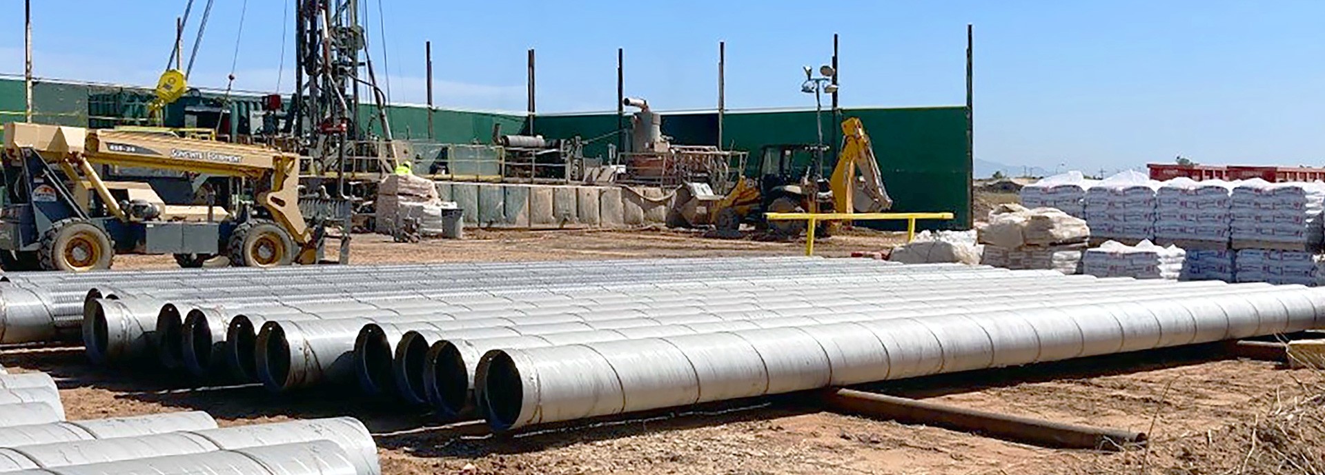 drill pipes laying on desert ground with construction area in the background and blue sky