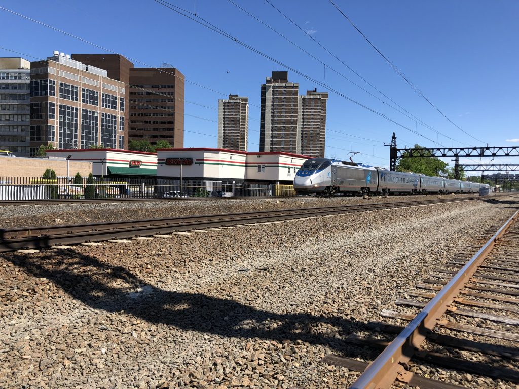 train coming from right on tracks with buildings in the background