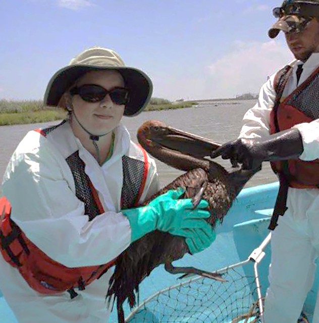 woman and man holding a pelican covered in oil on a boat on the gulf
