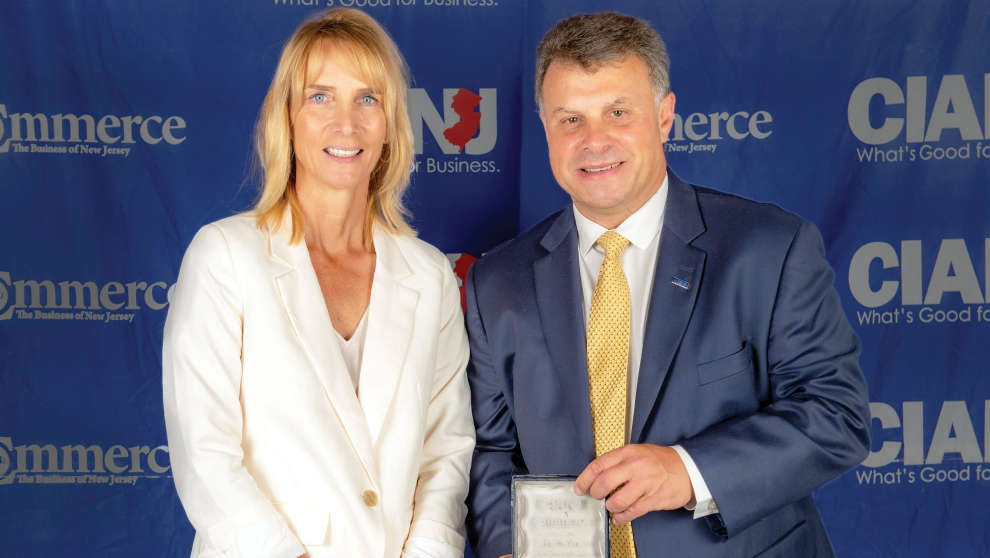 jayne warne and cianj man in front of step and repeat holding award