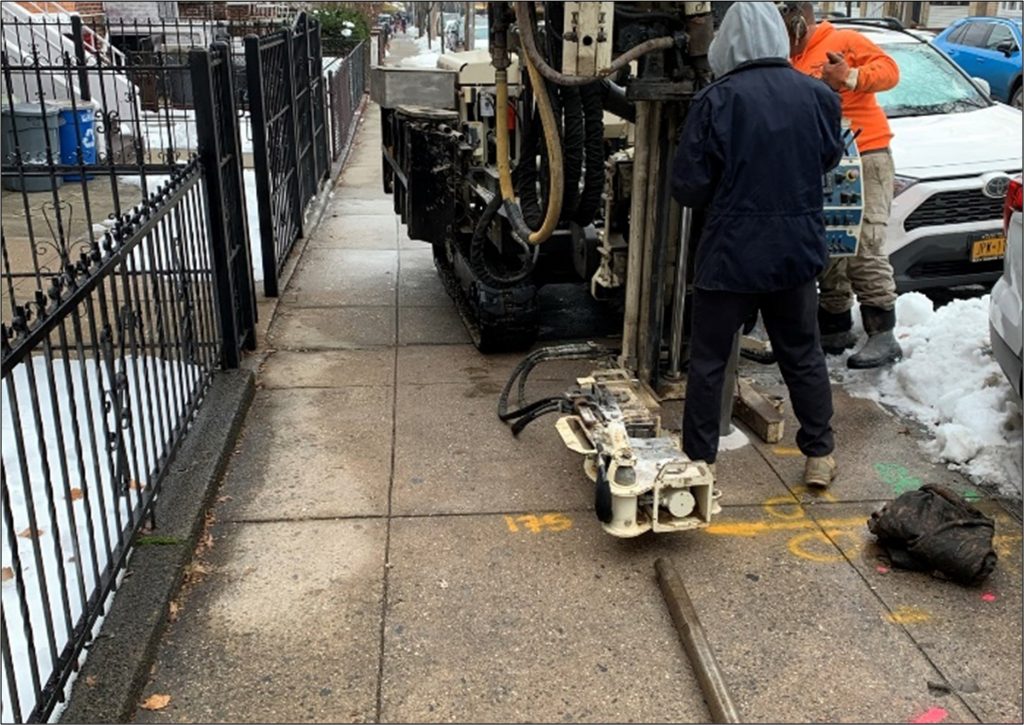equipment cutting sidewalk with metal fence on left
