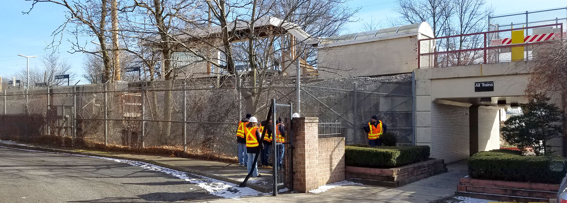 people in high vis vests and hard hats walking into a building with chain link fences and trees