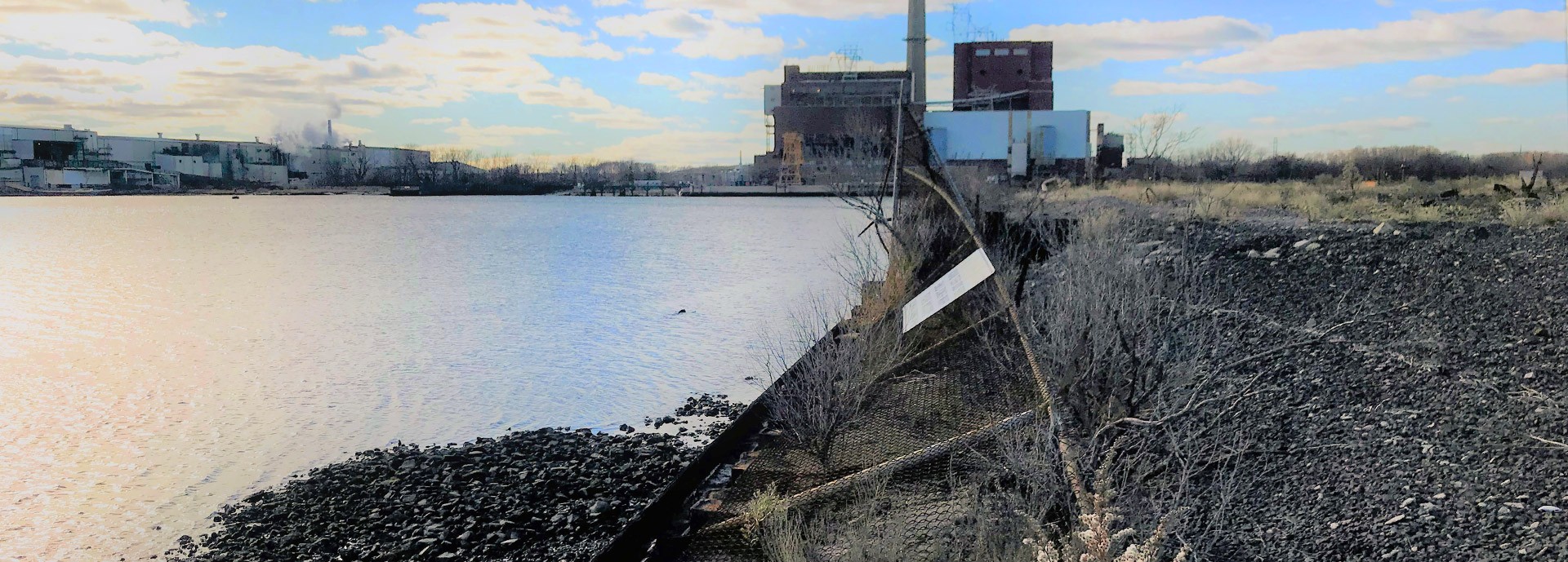 south bulkhead on shoreline with downed chain link fence, water on left and building in background and grasses on right