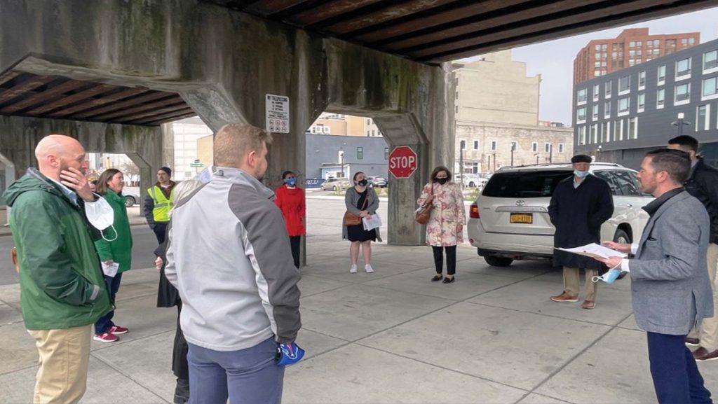 group of people under an overpass in a circle in syracuse ny with one man reading from a paper