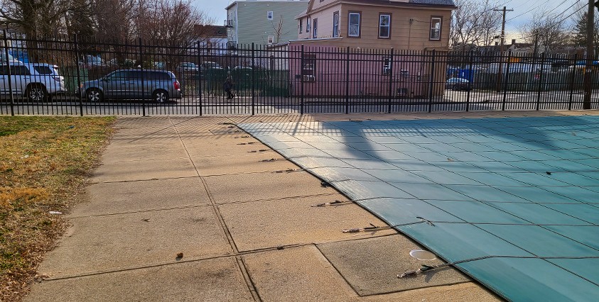 sidewalk and covered pool at sunset with metal fence and house in background