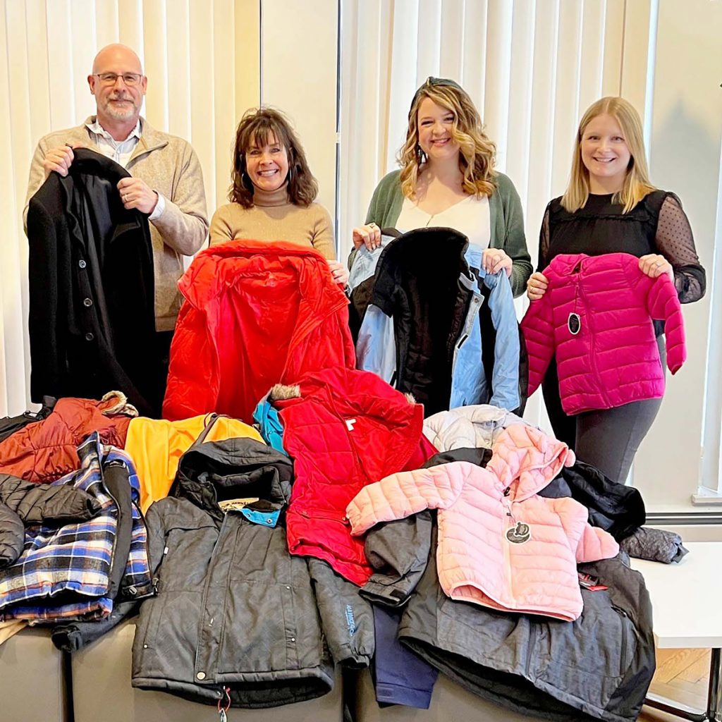 4 matrix employees holding up coats and standing behind a pile of coats