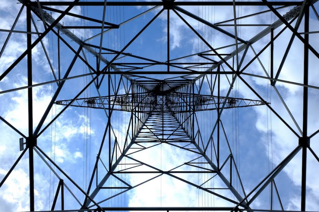 view from under an electrical tower looking toward sky with crossing metal bars